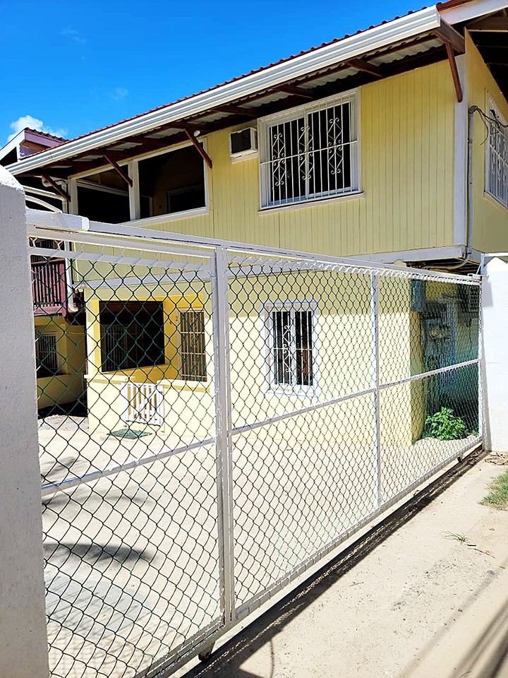 Exterior of a two-story yellow house with a white metal fence and security bars on windows