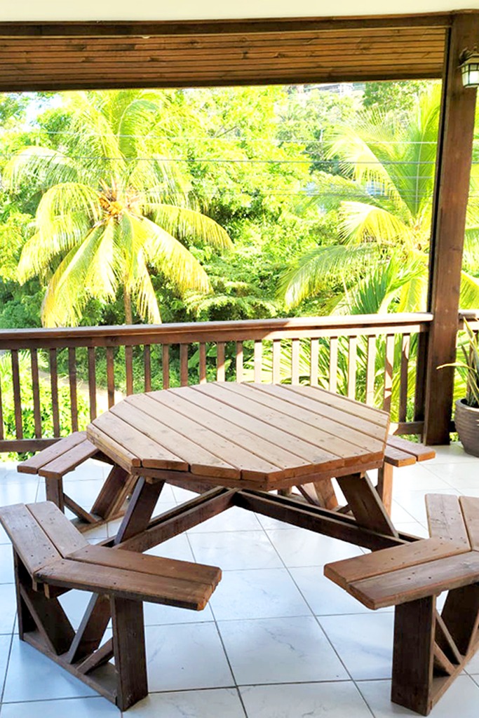 Outdoor wooden deck with a picnic table, benches, and lush greenery in the background