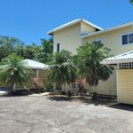 Large colonial-style home with a light yellow exterior, lush greenery, and a spacious driveway.