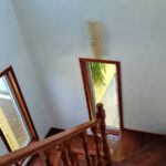 Interior Staircase View – A wooden staircase with a polished railing inside a well-lit house, featuring multiple windows with wooden trim.