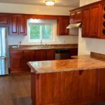 Kitchen Image: A kitchen with wooden cabinetry, granite countertops, a stainless steel refrigerator, and a small window above the sink.