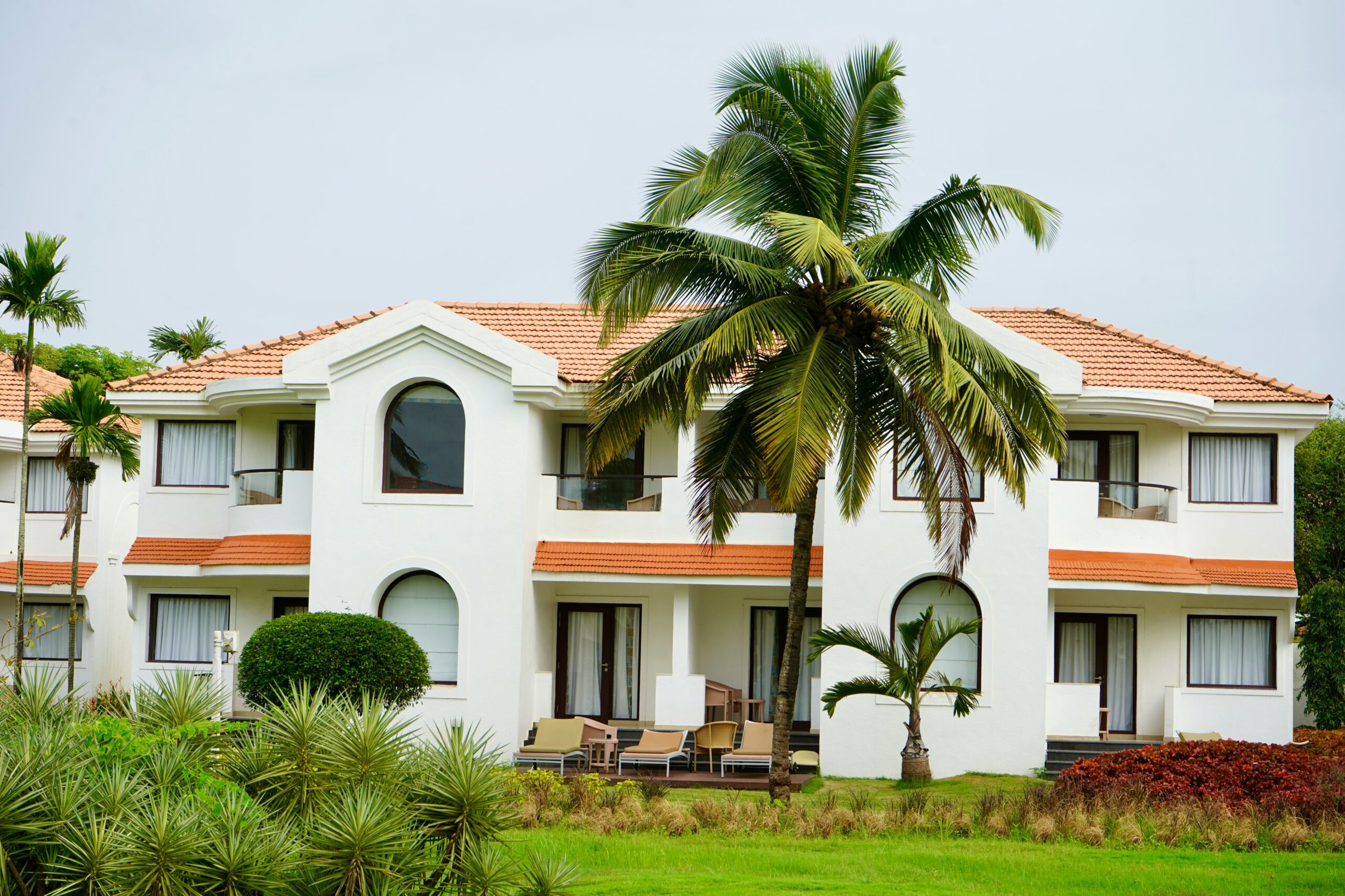 A luxurious white villa with terracotta roof tiles, surrounded by palm trees and greenery.