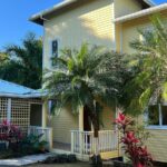 Yellow House Exterior with Palm Trees: A two-story yellow house with tropical landscaping, palm trees, and a covered porch.