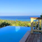 Infinity Pool with Ocean View: A serene infinity pool on a wooden deck overlooking the ocean and lush greenery.