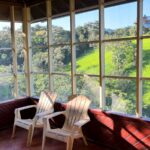 Screened Porch with Chairs: A cozy screened-in porch with two white chairs overlooking lush green hills and trees.