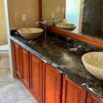 Bathroom Vanity with Vessel Sinks: A bathroom vanity featuring a dark marble countertop, wooden cabinetry, and two stone vessel sinks.