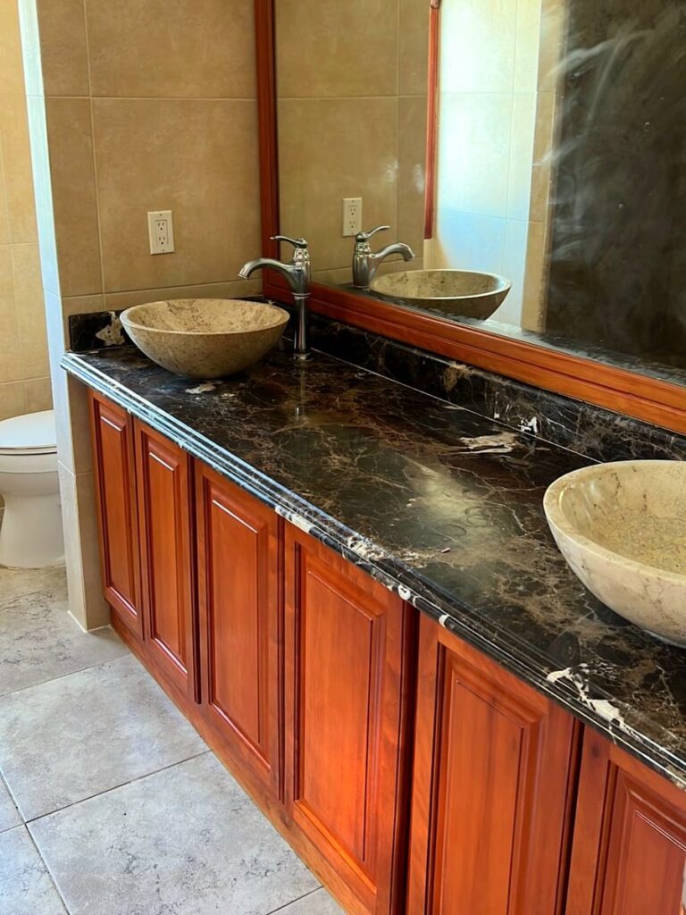 Bathroom Vanity with Vessel Sinks: A bathroom vanity featuring a dark marble countertop, wooden cabinetry, and two stone vessel sinks