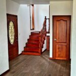 Wooden Staircase Image: A wooden staircase with decorative railings next to a glass-paneled front door and a small window.