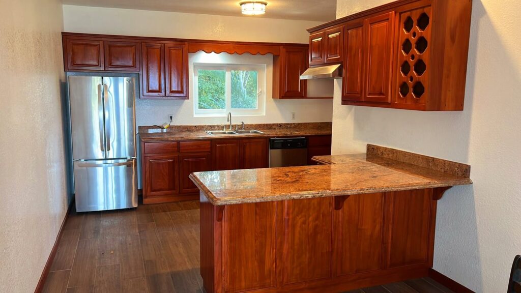 Kitchen Image: A kitchen with wooden cabinetry, granite countertops, a stainless steel refrigerator, and a small window above the sink